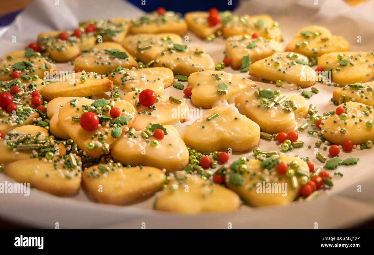 closeup view over a tray of fresh baked homemade christmas cookies, shape of hearts, decorated with sugar coating and colorful sugar beads, backlight, Stock Photo