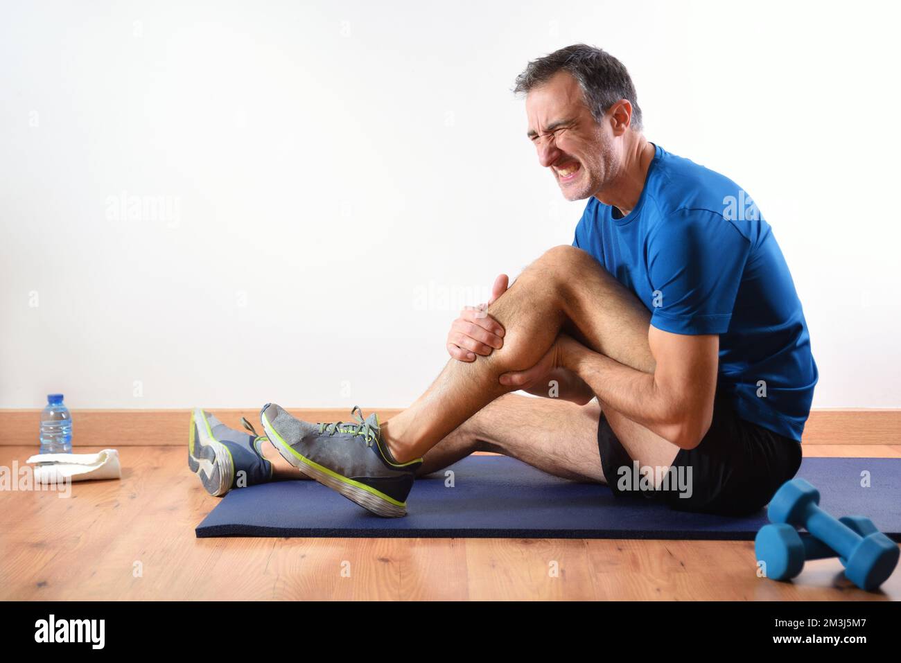 MMan doing sports indoors complaining with leg pain sitting on a mat. Side view Stock Photo Alamy