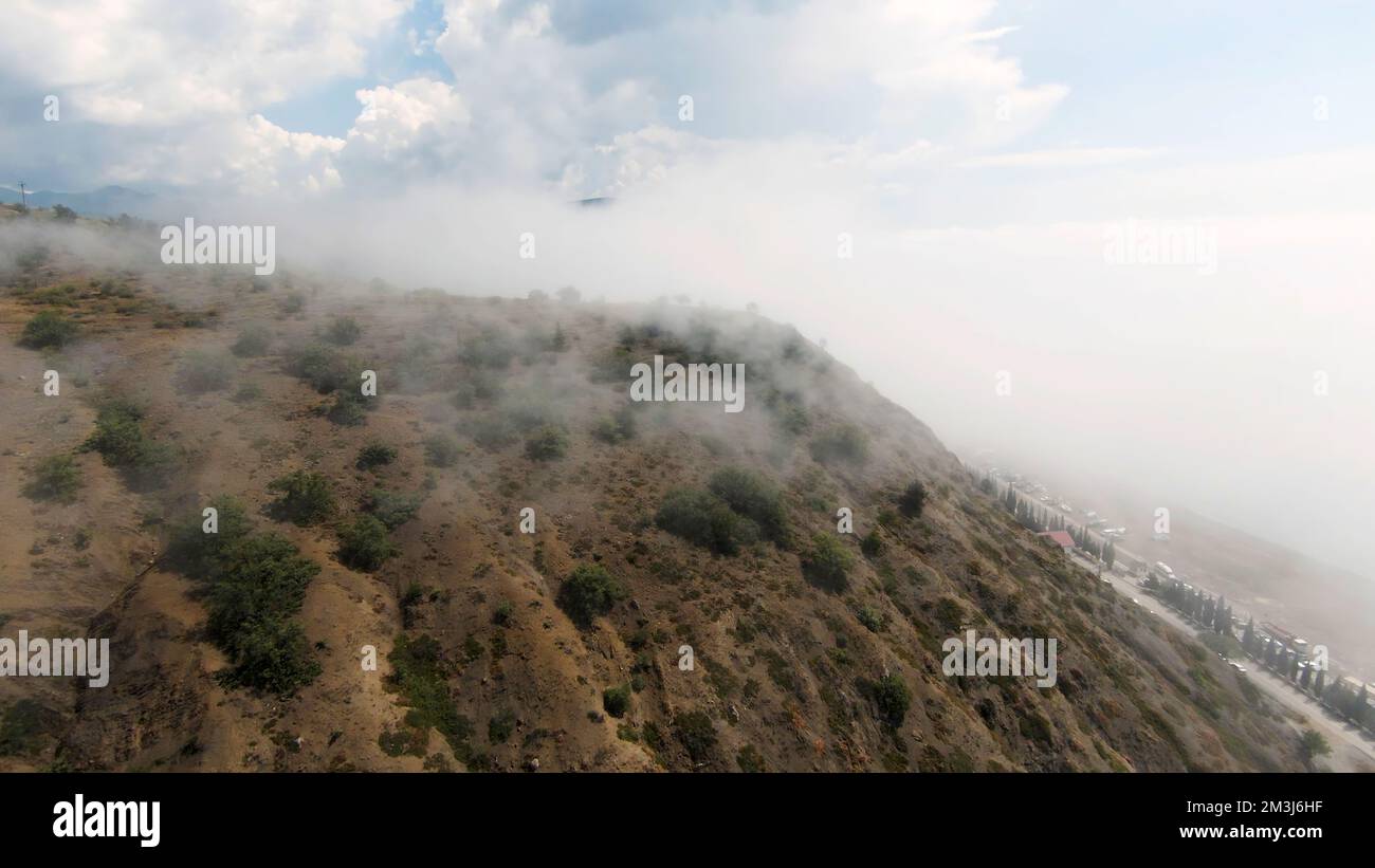 Heavy fog over mountain forest, aerial view. Shot. Picturesque landscape with green grass and bushes Stock Photo