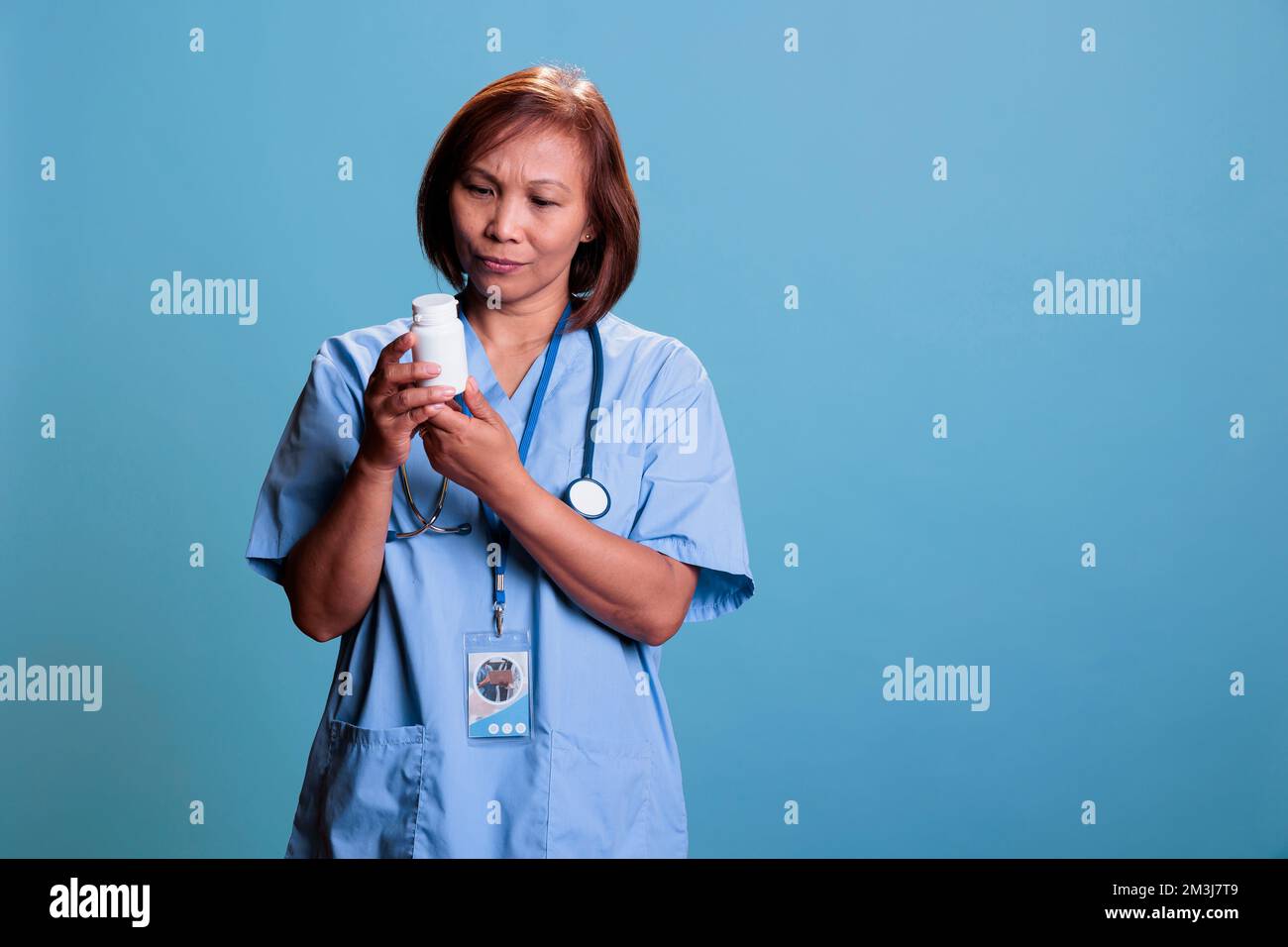 Serious asian nurse working at medication treatment to prevent patient disease, holding drugs box reading pharmaceutical leaflet in studio with blue background. Health care service and concept Stock Photo