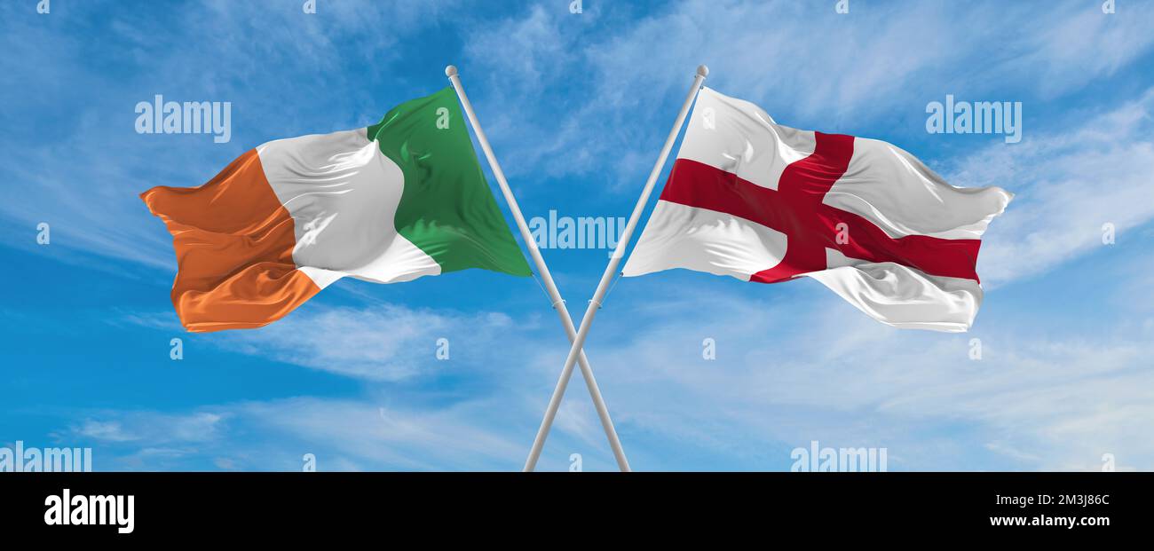 two crossed flags England and Ireland waving in wind at cloudy sky ...