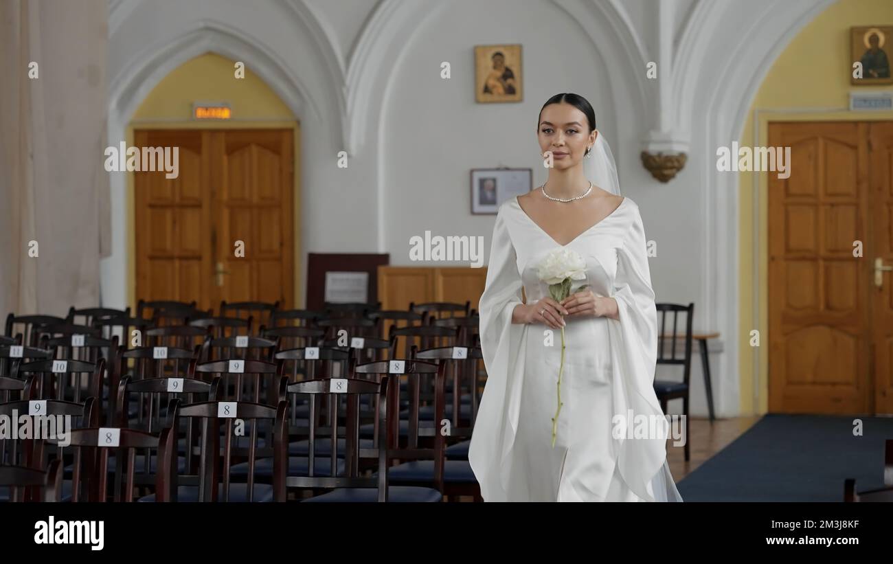Details of wedding ceremony. Action. Young caucasian woman walking along empty rows of a chapel Stock Photo