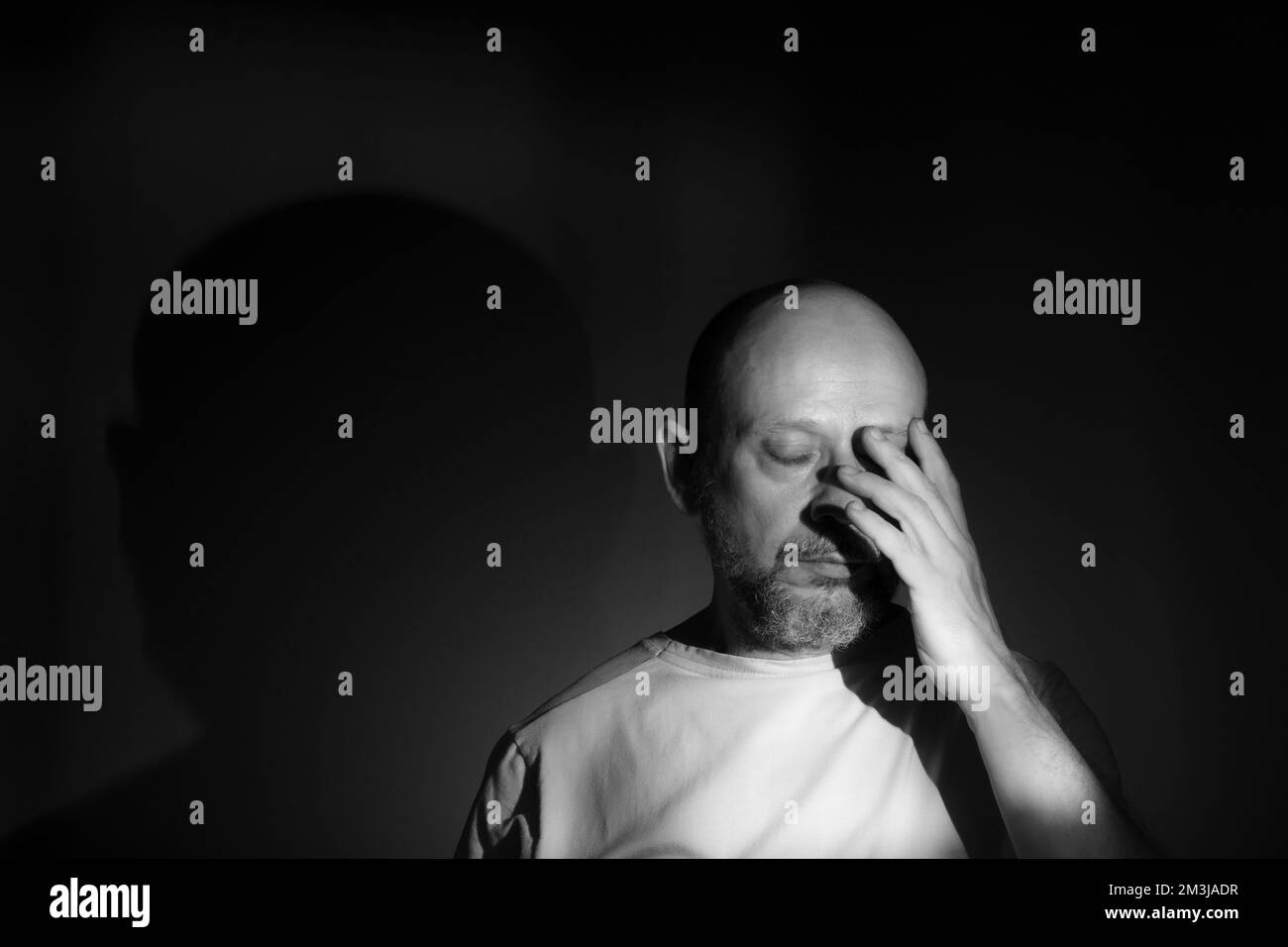 Black and white portrait of depressed middle age man with hand on face isolated on black background having financial problems or suffering from loneli Stock Photo