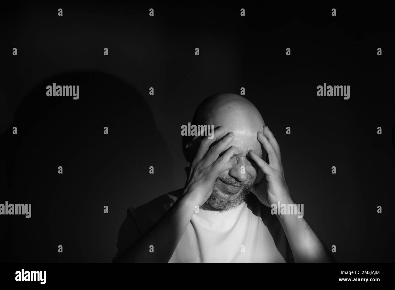 Black and white portrait of depressed middle age man with hand on face isolated on black background having financial problems or suffering from loneli Stock Photo