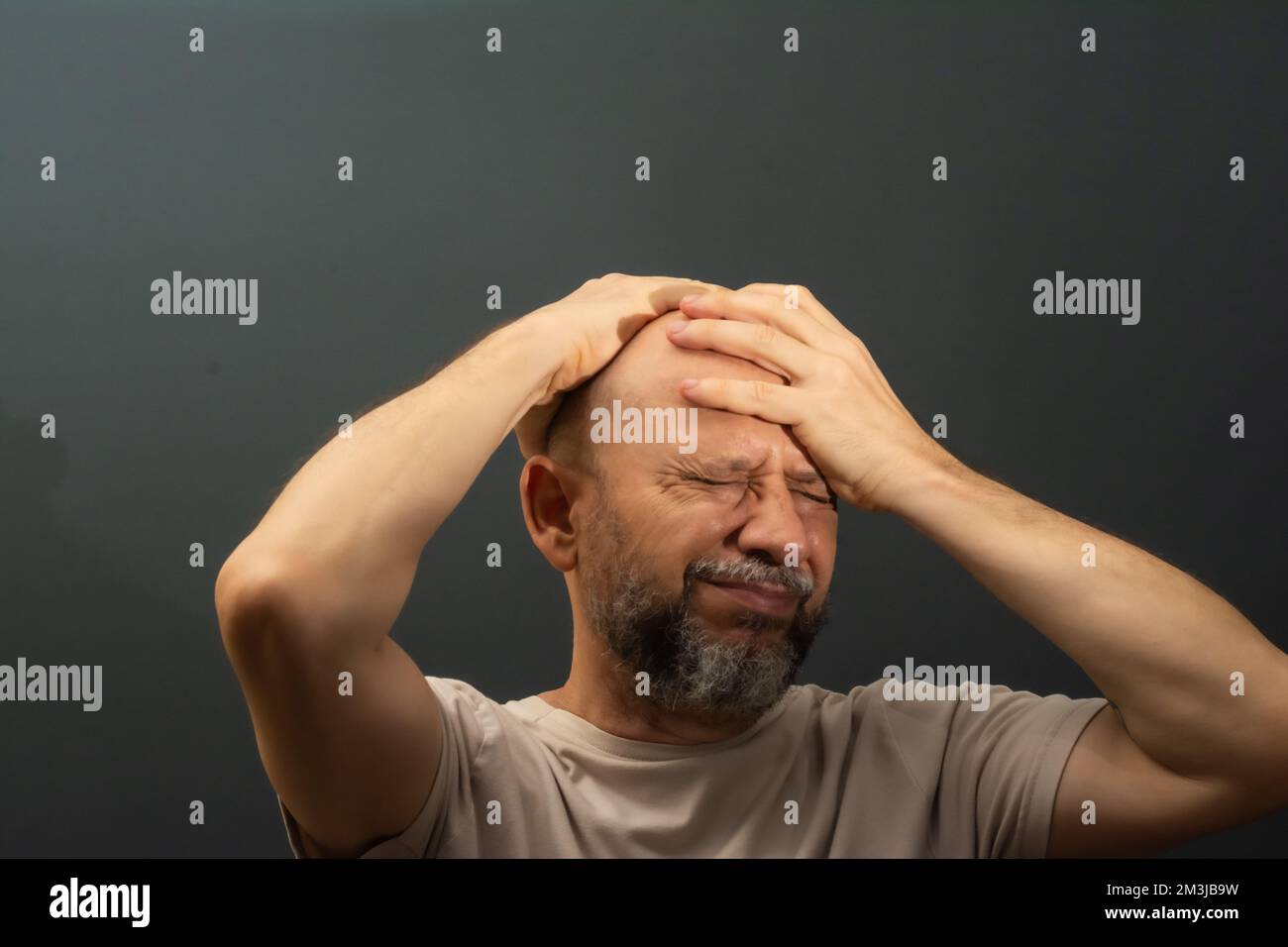 Depressed middle-aged man with both hands on his head isolated on gray ...