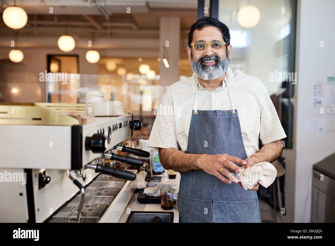 Smiling mature owner with eyeglasses standing by espresso machine Stock