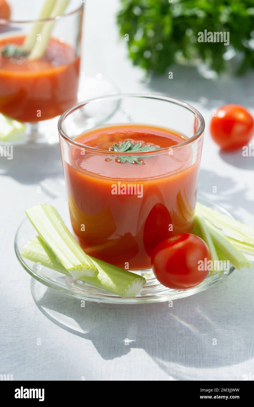 Two glasses with fresh tomato juice, celery, parsley and ripe tomatoes