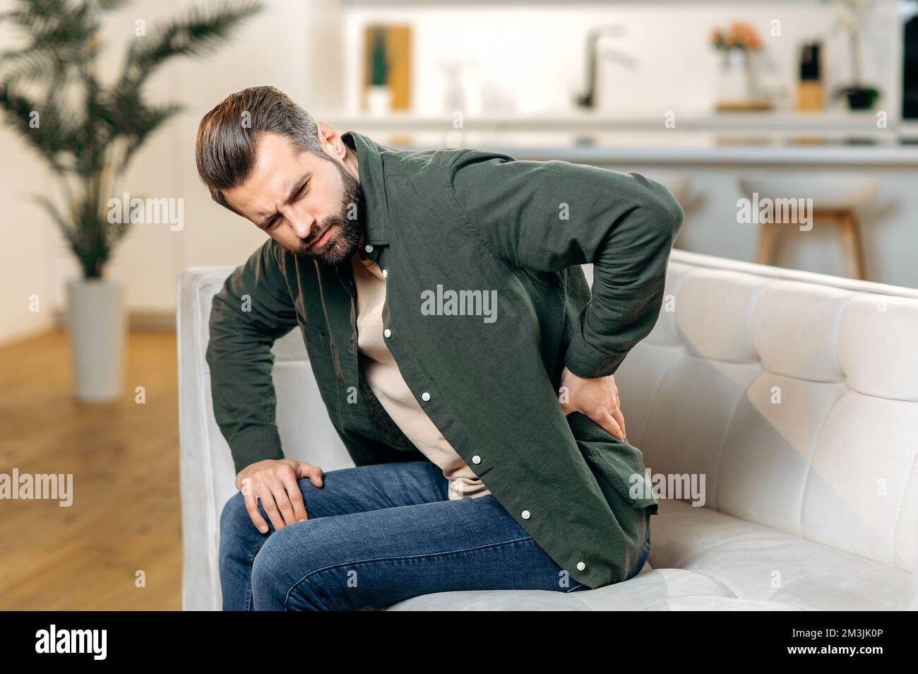 Back problems concept. Sad caucasian man, in casual wear, sit on sofa