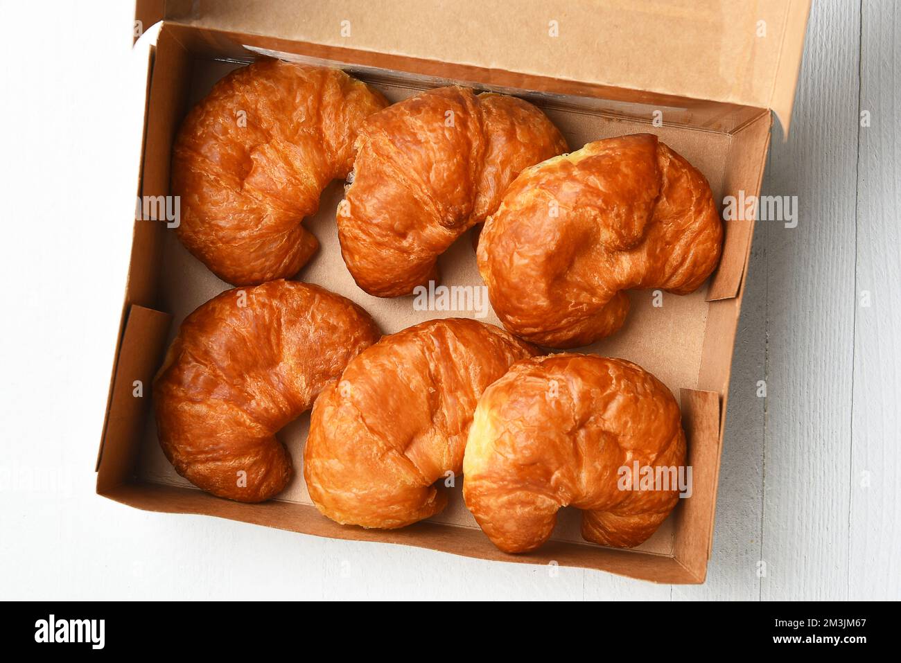 High angle shot of six fresh baked Croissants in an open bakery box. Stock Photo