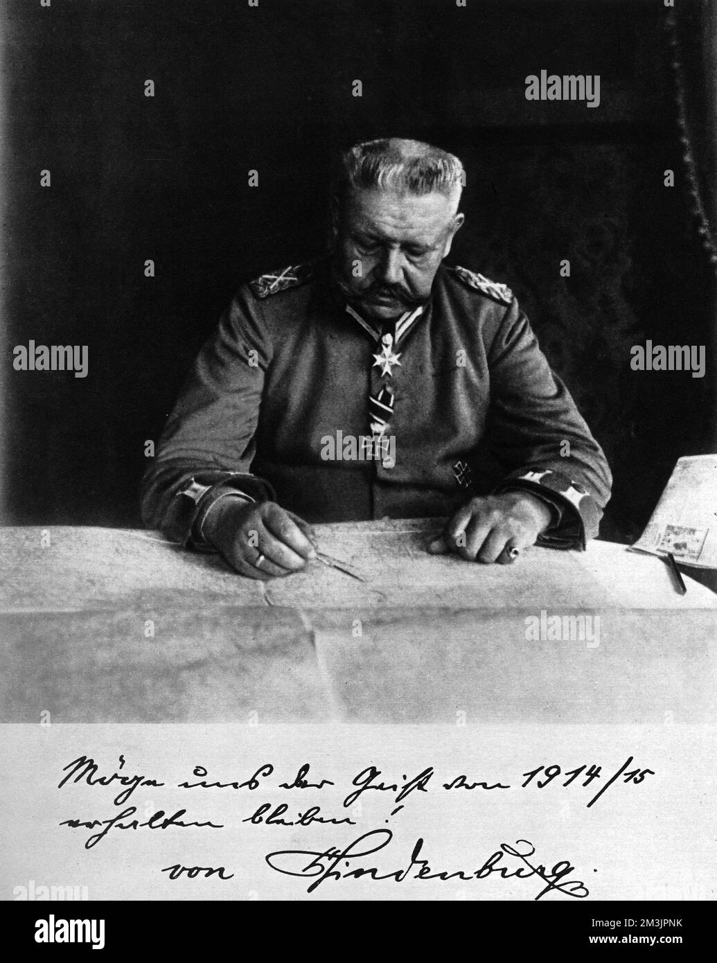 Marshal Paul von Hindenburg (1847 -  1934), sitting at a strategic map. A veteran of the Franco-Prussian War, he was recalled from retirement on the outbreak of World War I, winning decisive victories on the Eastern front at Tannenburg (1914) and the Masurian Lakes (1915). He became Chief of Staff of the Third Army in August 1916, forming with Ludendorff the Third Supreme Command. The inscription at the bottom of the picture reads: 'May the spirit of 1914-15 remain with us - Von Hindenburg'.     Date: 1915 Stock Photo