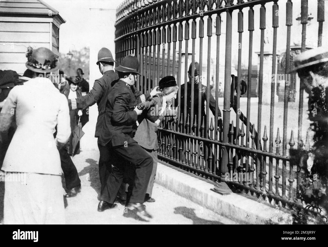 A protesting suffragette is forcibly removed from the railings of Buckingham Palace by policemen     Date: 1914 Stock Photo