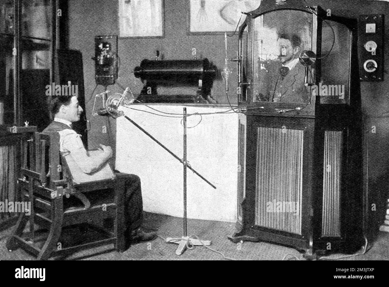 A photograph of an x-ray in progress where the doctor is protected by a lead lined cabinet. An invention by MM. Radiguet and Massiot, it enabled doctors to control x-rays without exposure to excessive radiation.     Date: 1910 Stock Photo