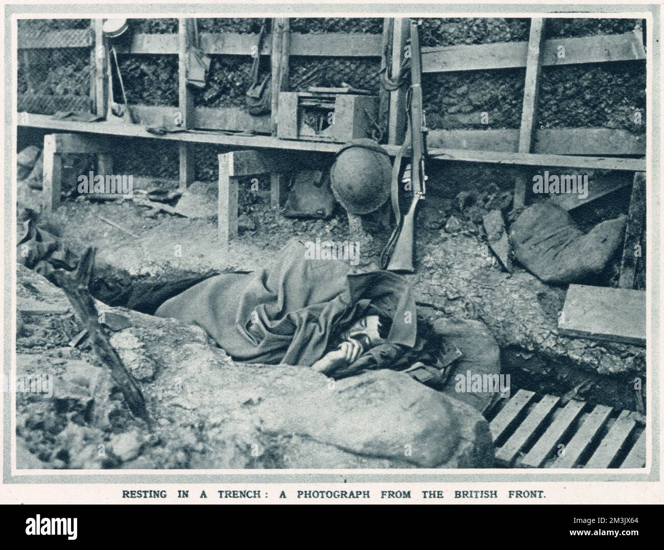 A British soldier, his rifle and helmet beside him, sleeps in the uncomfortable surroundings of his trench. Stock Photo