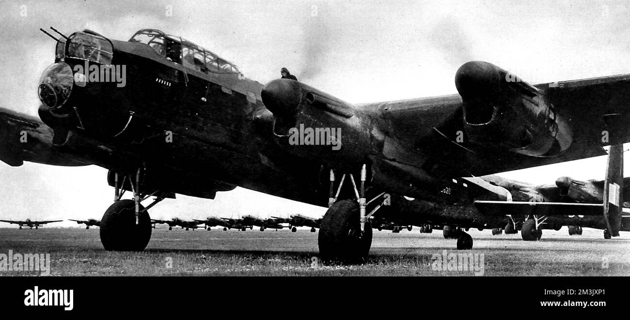 Avro Lancaster heavy bomber at a British airfield, ready to take off, somewhere in England.  Although the engines are already running, one of the aircrew can be seen standing on the port wing, perhaps carrying out final checks.  In the background, one can see the other Lancasters of this squadron, also ready to go.     Date: 1942 Stock Photo