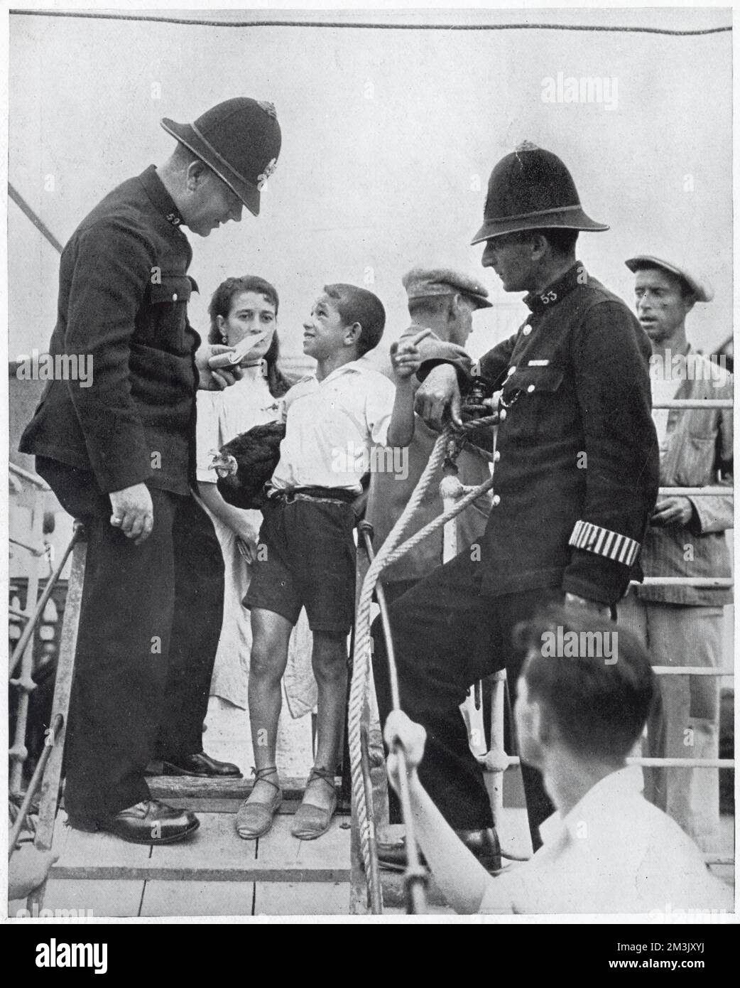 Two members of Gibraltar's police force questioning a Spanish boy on the gang-way of a refugee boat, August 1936.   The Spanish Civil War, which started in the summer of 1936, meant that thousands of Spaniards became refugees, some finding sanctuary in Gibraltar, others heading for France. By August, the British authorities had to shut their border with Spain to refugees to prevent an epidemic sweeping through those refugees who had already arrived. Stock Photo