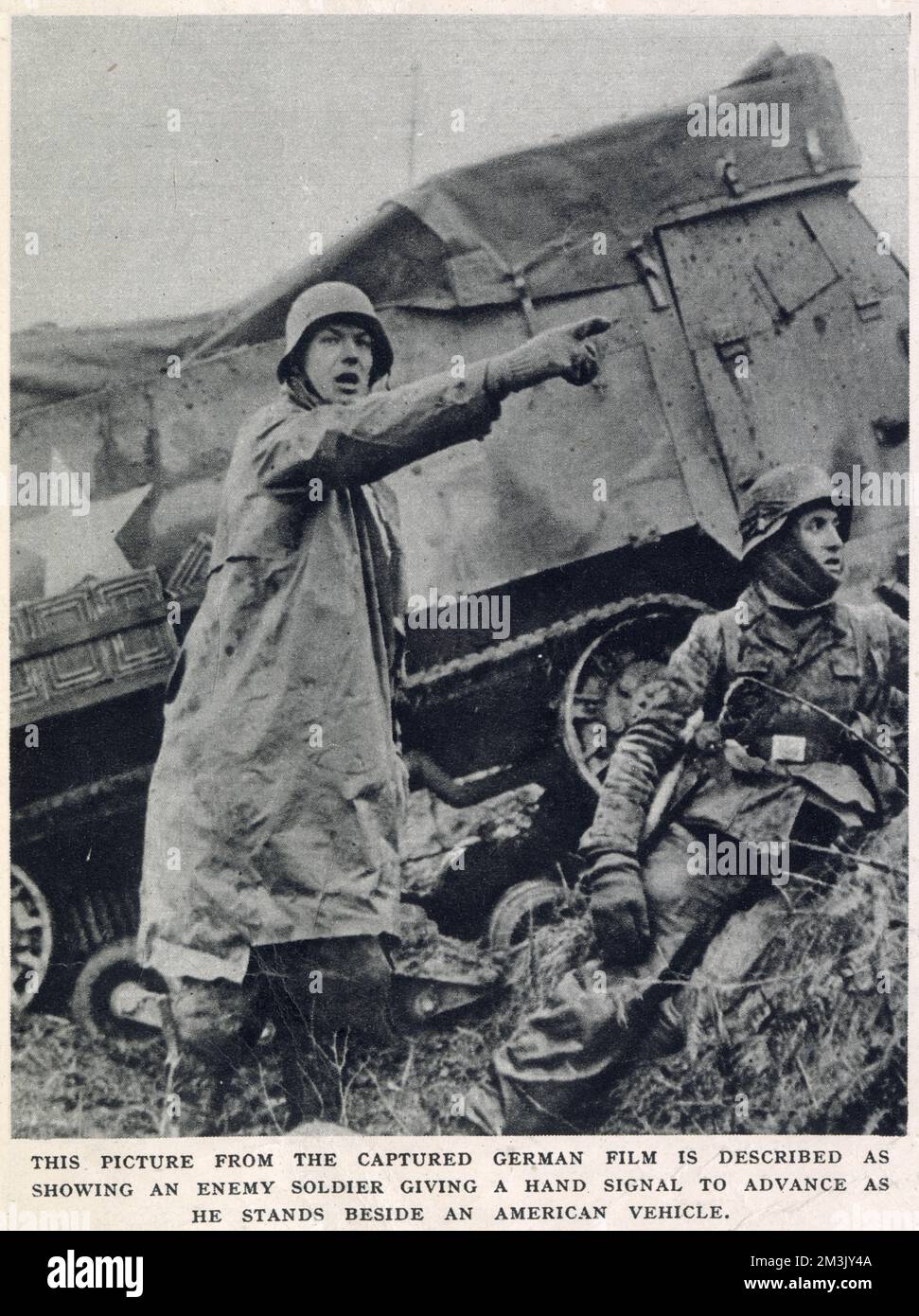 German soldier signalling to his comrades during the early stages of the 'Battle of the Bulge', December 1944. Behind is a knocked-out American half-track.  The 'Battle of the Bulge' was the last major Nazi offensive on the Western front during the Second World War and, though initially successful, resulted in major German losses.  This photograph was taken by a German film unit during the German offensive. The film was then captured during the Allied counter-offensive.     Date: 1944 Stock Photo