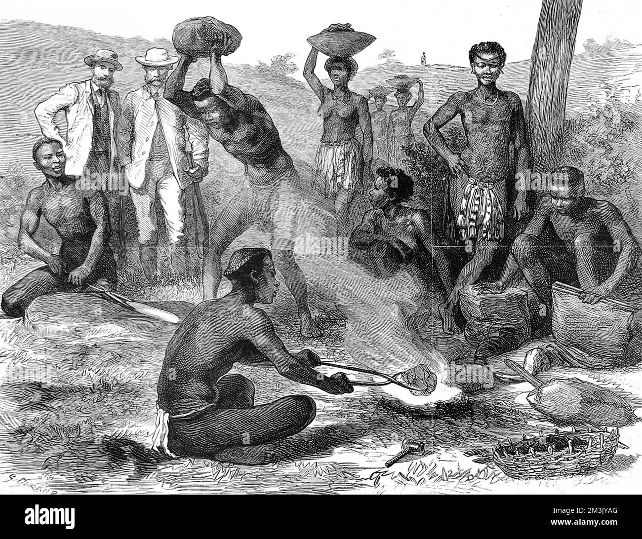 Scene depicting a Zulu making a spear in a fire and shaping it into the famous zulu weapon. Male and female zulus are in the foreground, while two European men watch in the background.  1879 Stock Photo