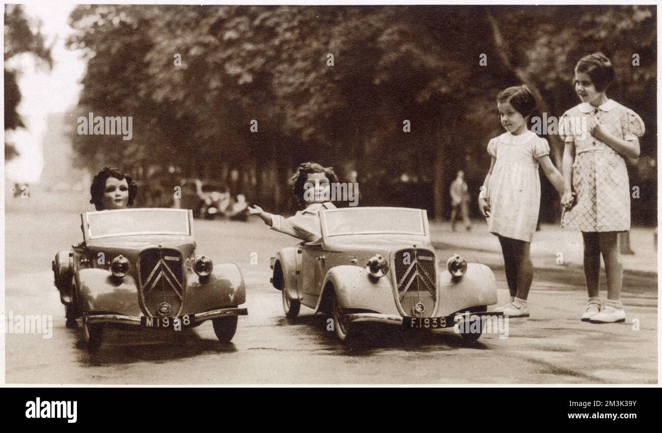 Two model cars offered 'by the children of France' to Princess Elizabeth and Princess Margaret, pictured with two dolls 'Marianne' and 'France' sitting in them and two young French girls looking on, 1938. Stock Photo