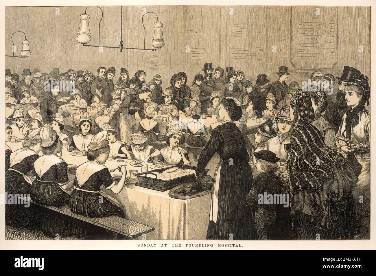 This is a scene on sunday at the Foundling Hospital where orphans are sitting down to a meal on long tables and being served by young women in aprons and caps. In the foreground, wealthy looking patrons appear to be witnessing the scene. Stock Photo