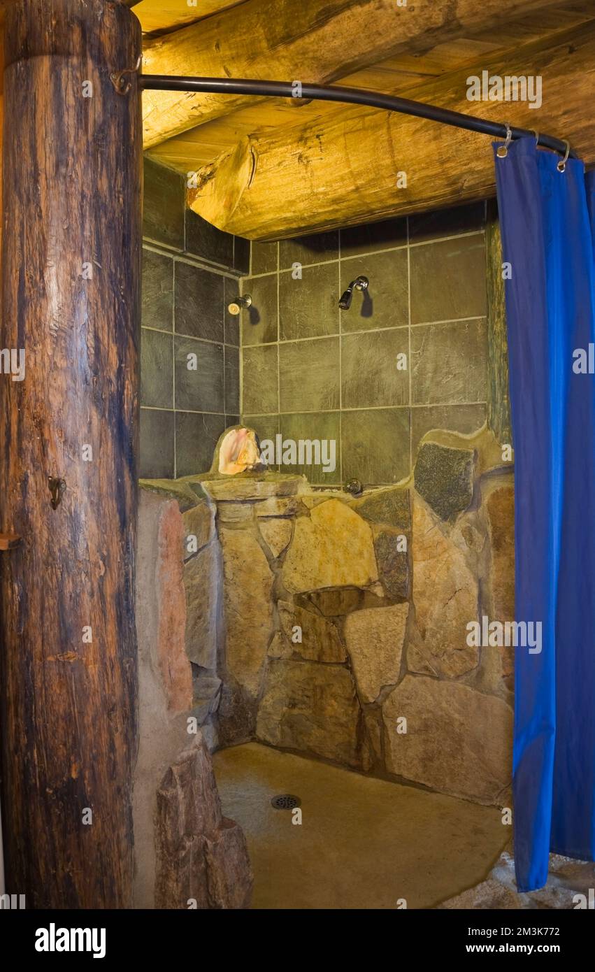 Natural stone and ceramic shower stall with blue curtain inside rustic log cabin. Stock Photo