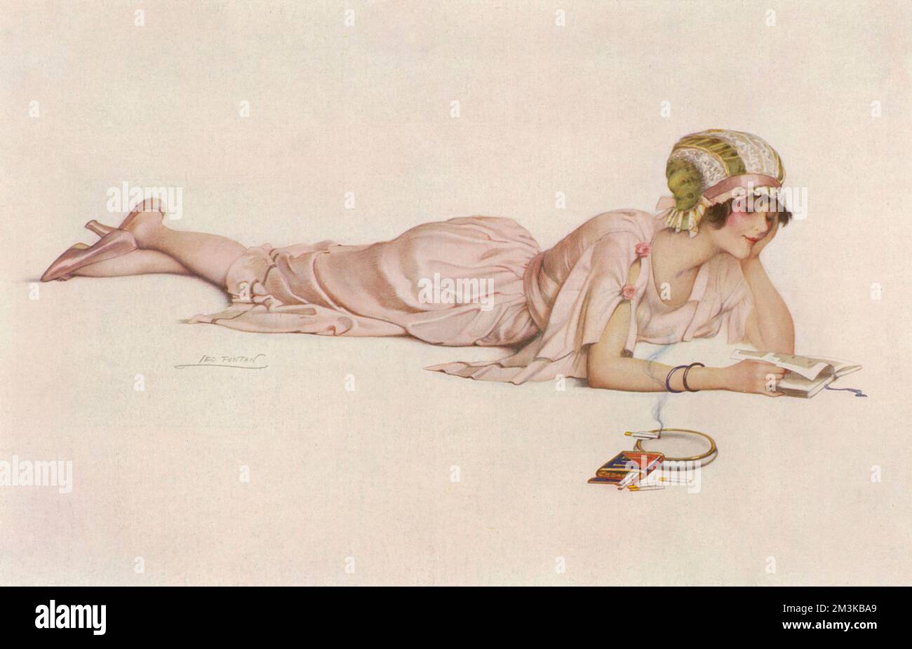 A contented looking young woman, wearing a lovely pink, silk dress, matching shoes and lace cap, enjoys some me-time as she reads a book lying flat on her stomach and smokes like a chimney.     Date: 1920 Stock Photo