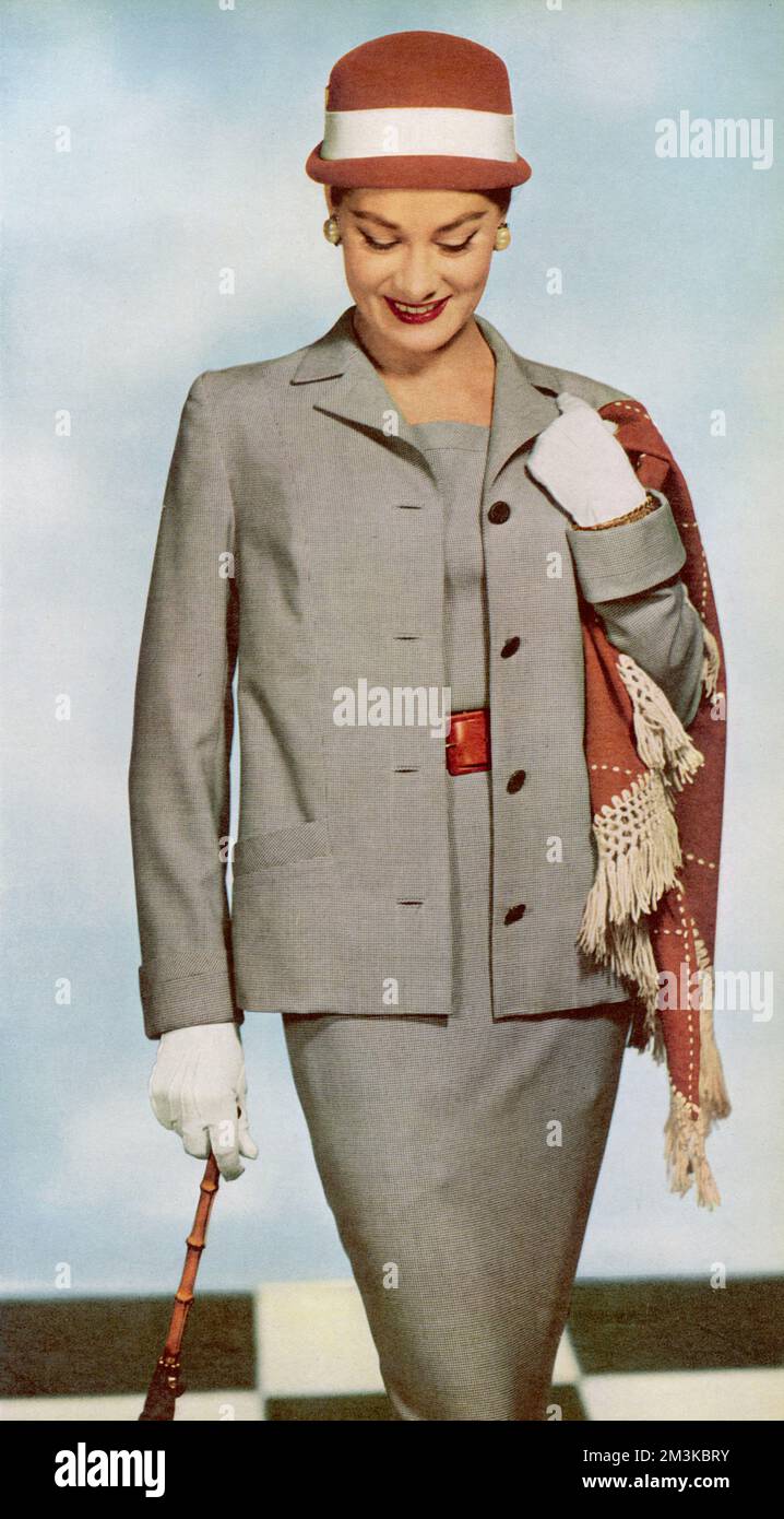A sleeveless square necked slim dress with a boxy jacket made from the finest men's grey and white pinpoint suiting.  Worn with a red calf belt, the outfit costs 40 guineas from Harrods.  Accessories include a a tan brick felt topper with white petersham band, a triangle tan brick scarf in jersey with a string fringe and white gloves.     Date: 1956 Stock Photo