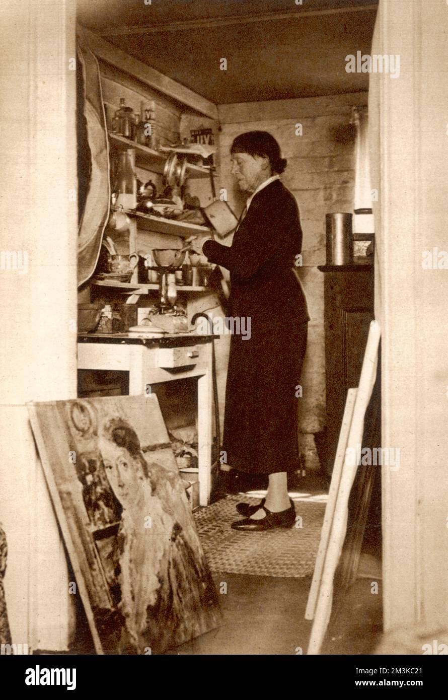 The artist Ethel Walker at her Buckinghamshire cottage. She is seen here in her kitchen cooking at the stove, flanked by her paintings which lean by the doorway.. Ethel was bombed out of her Chelsea studio in 1940 and after this date lived in extreme simplicity at her workman's cottage in Cholesbury.     Date: 1861-1951 Stock Photo
