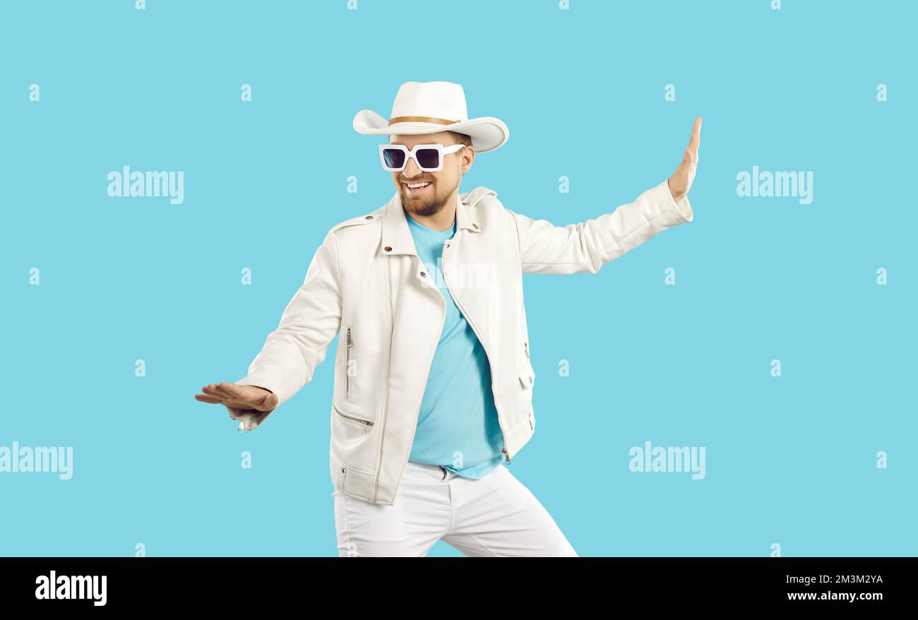Funny man in white leather jacket, hat and sunglasses dancing isolated on blue background Stock