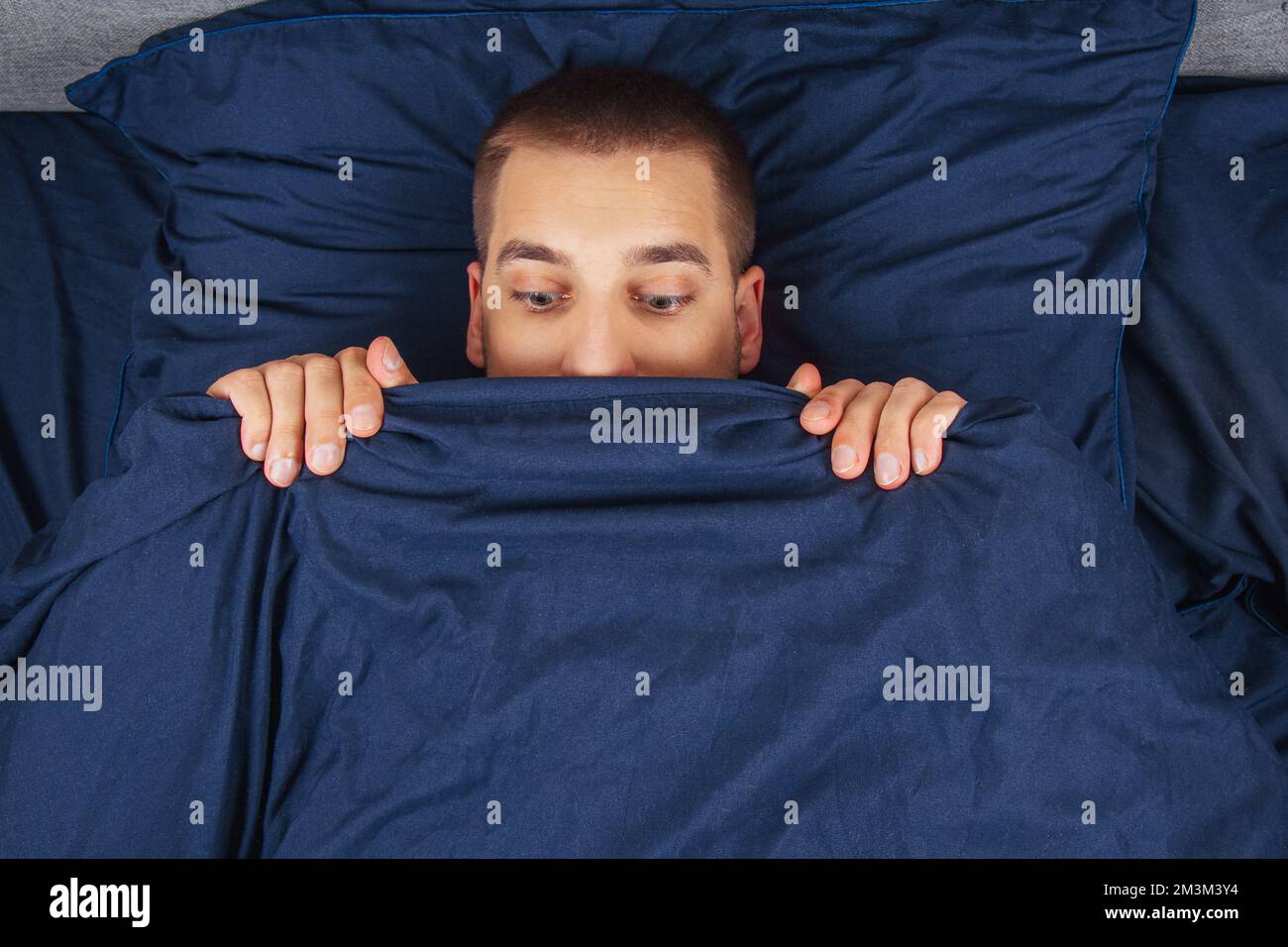 Look down. A handsome young guy hiding behind a blanket looks to the side. Direction of gaze in different directions. Stock Photo