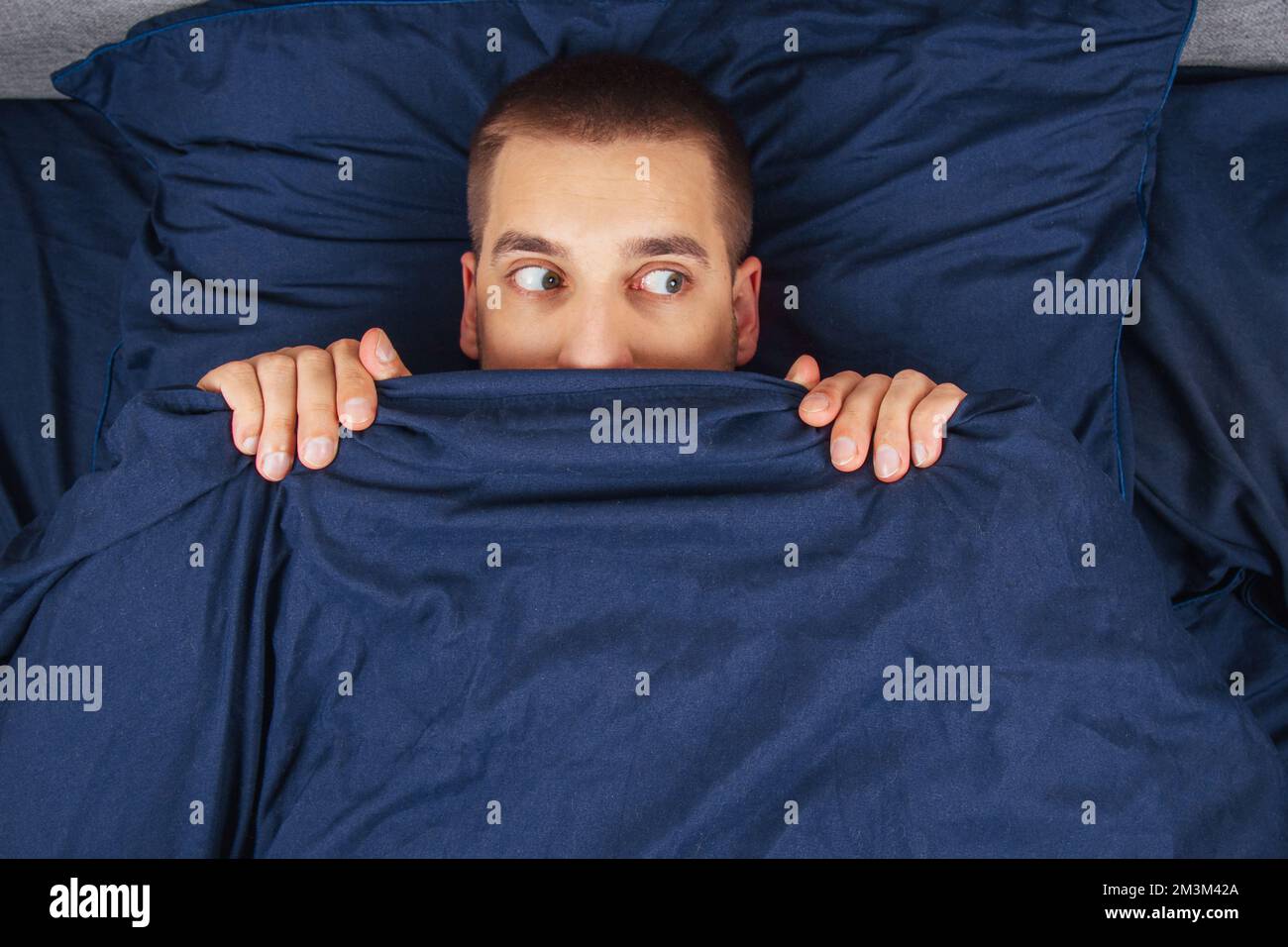 Look to the right. A handsome young guy hiding behind a blanket looks to the side. Direction of gaze in different directions. Stock Photo