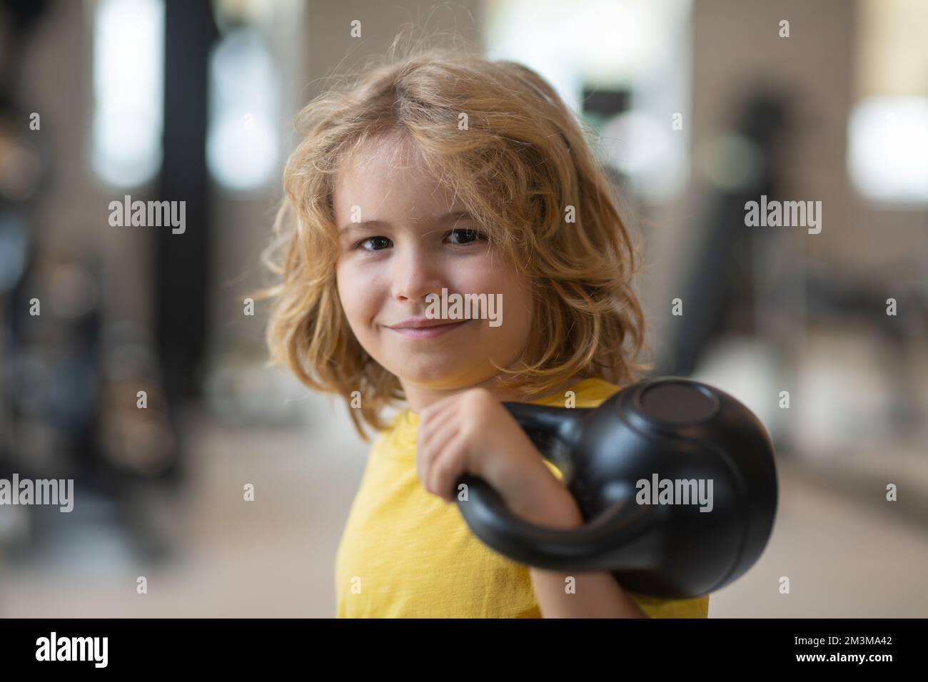 Kid workout kid in gym. Kid raising a kettlebell. Cute child training