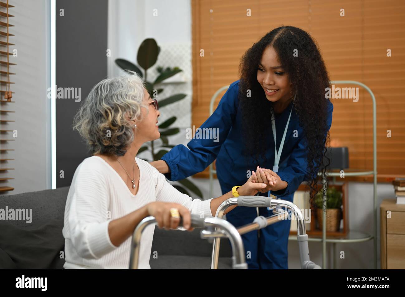 Attentive caregiver assisting, teaching senior woman to walk with walker. Assistance, rehabilitation and health Stock Photo