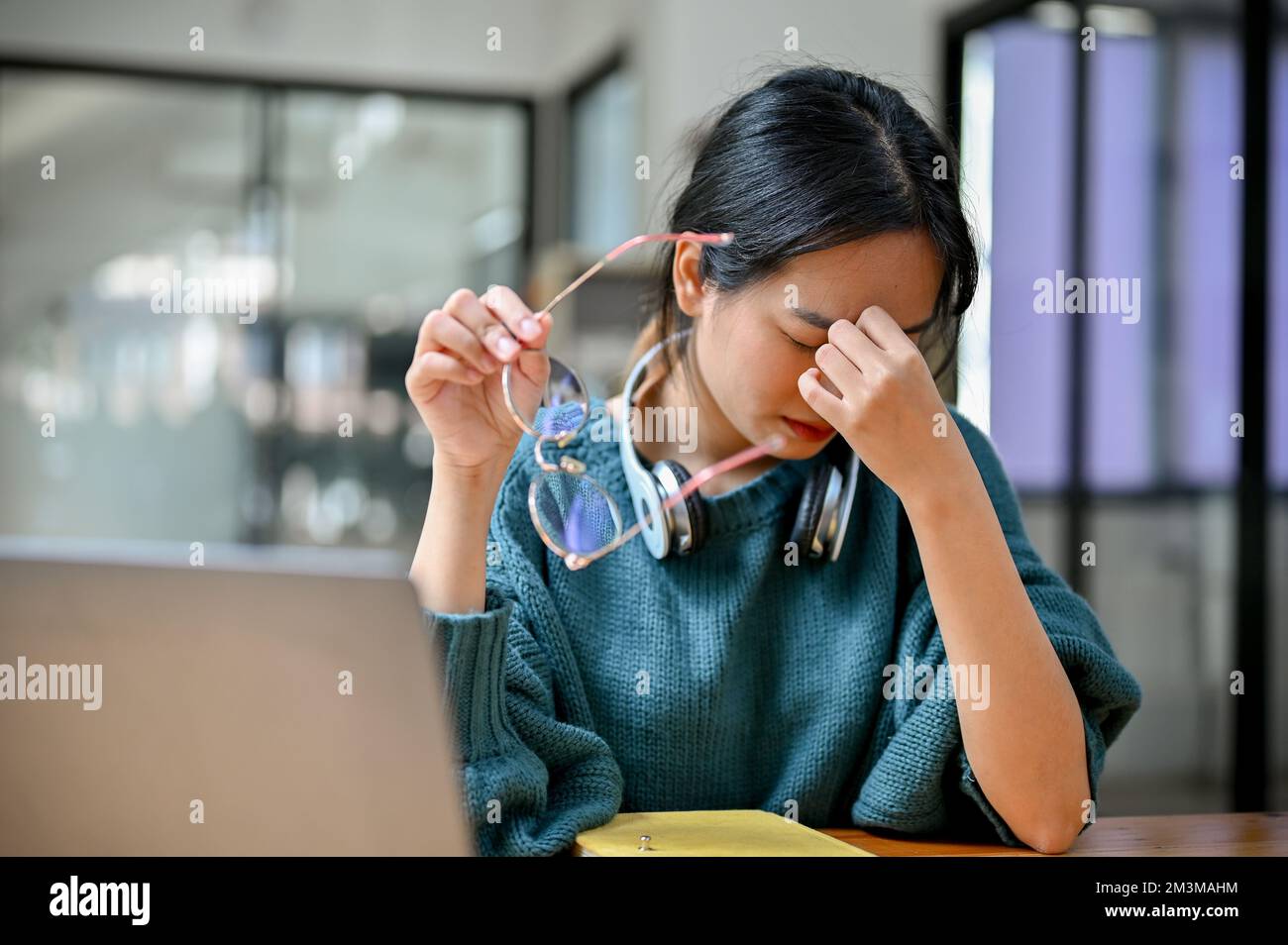 Young Asian female college student taking off her eyeglasses, suffering