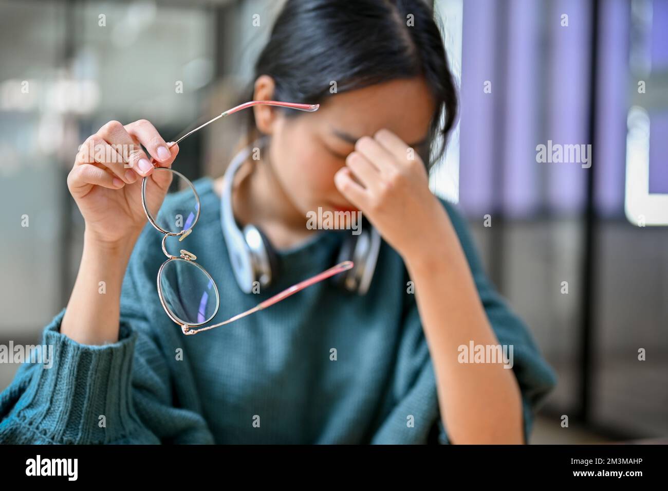 Young Asian female college student taking off her eyeglasses, suffering from eyes strain