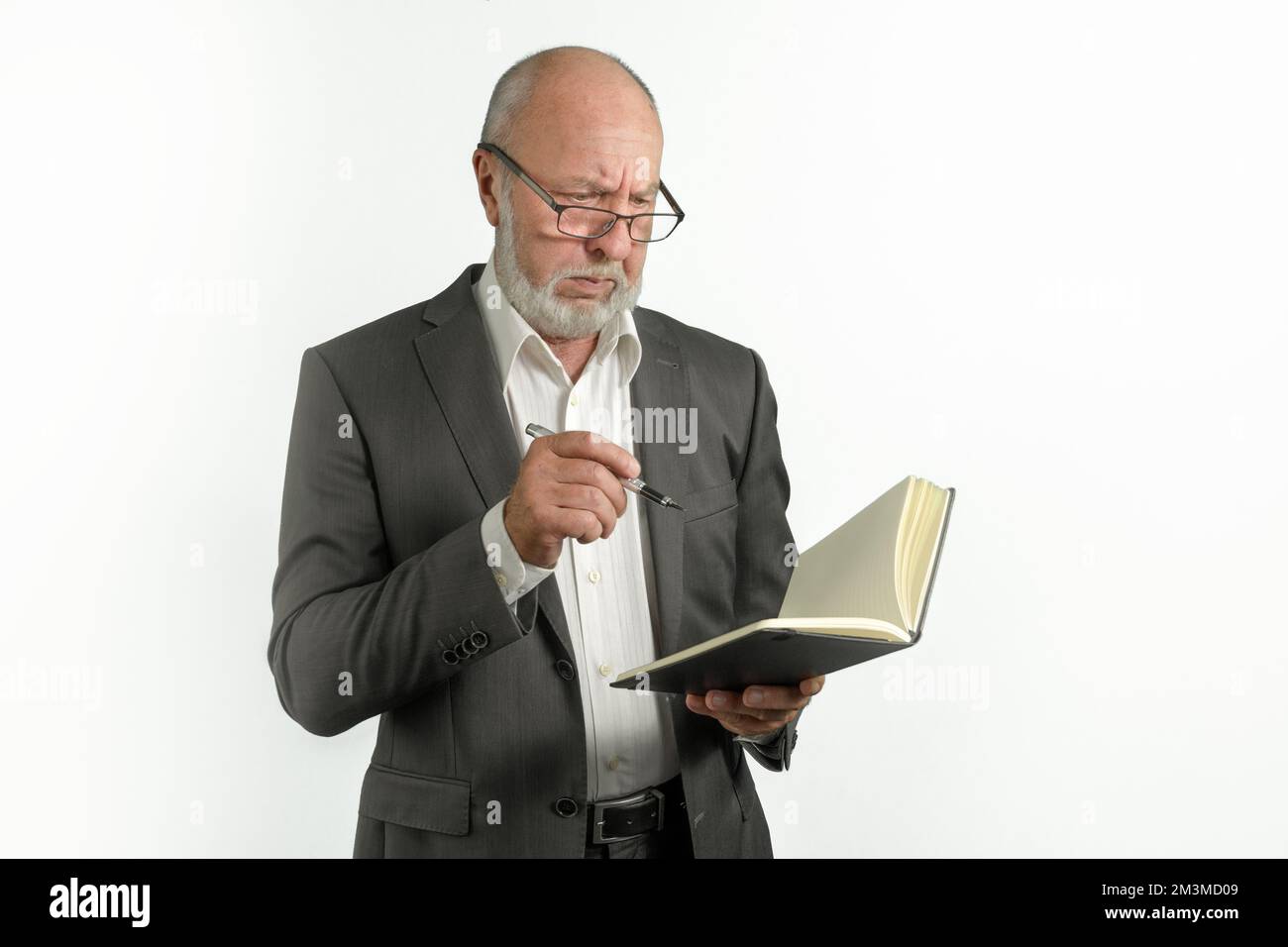 An elderly man in a suit with a notebook and a pen is thinking about a task. on a white background Stock Photo