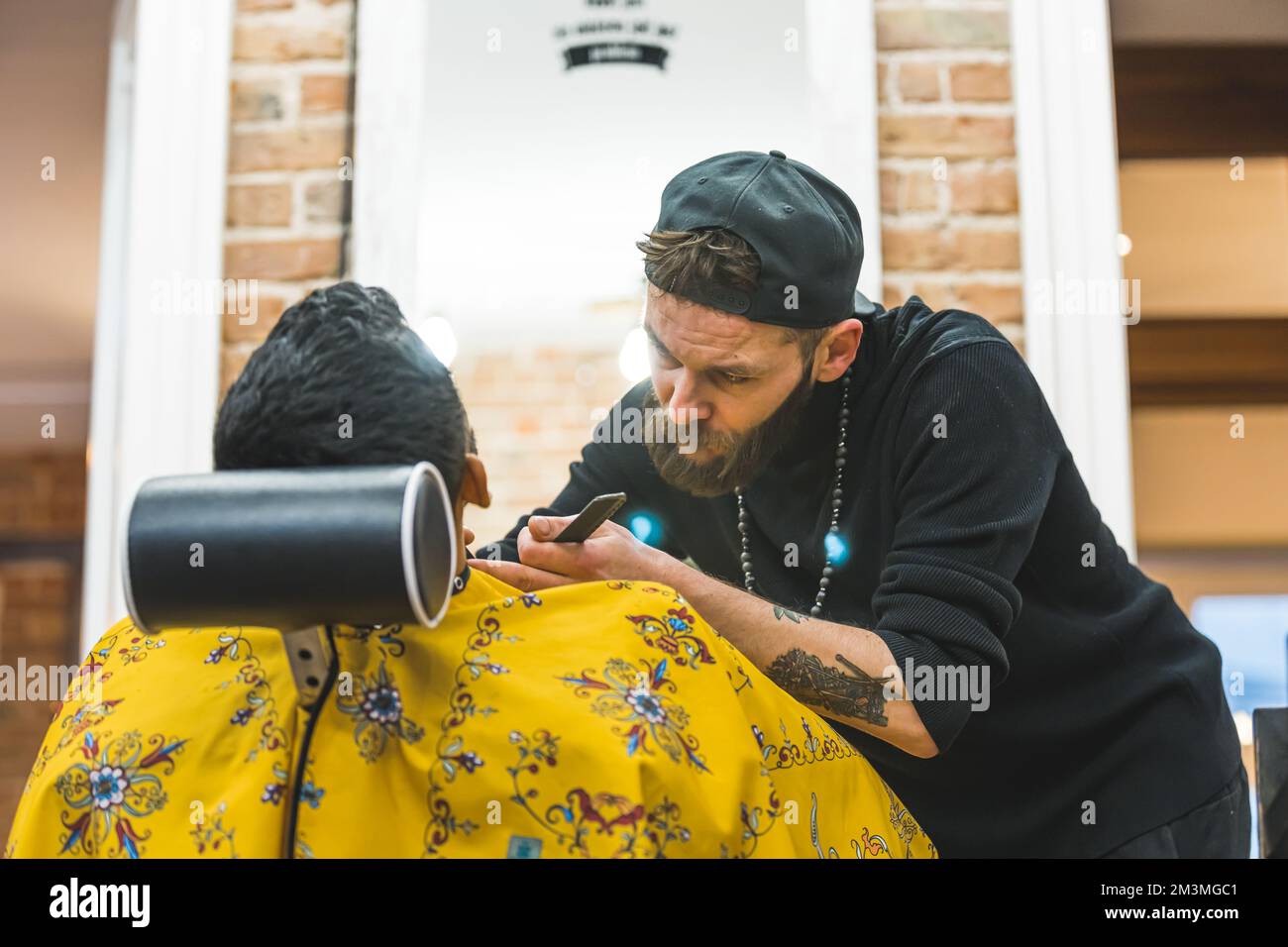 Back view of professional male barber with hat and tattoos trimming