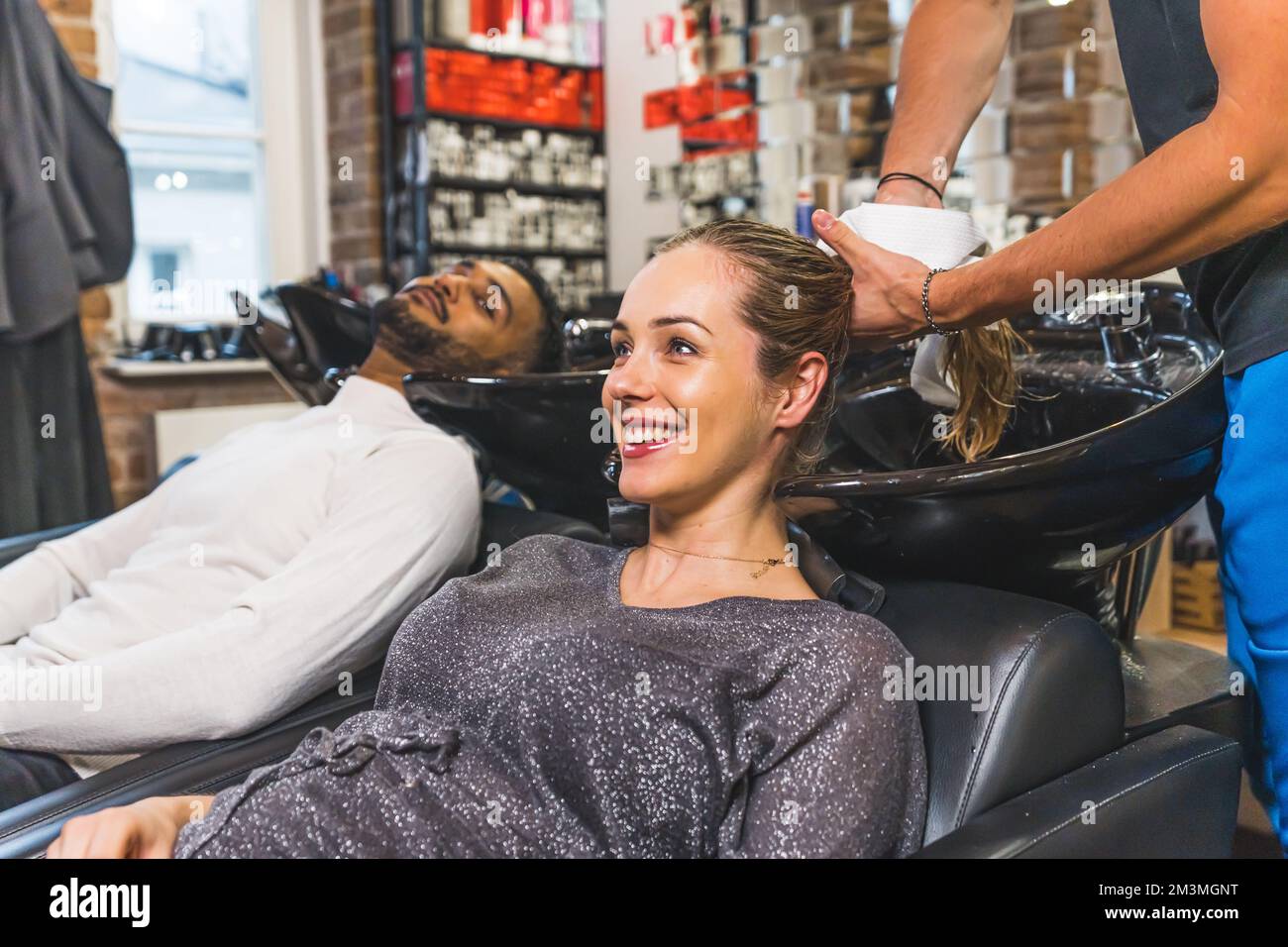Happy female blonde customer having her hair dryed with a towel by male hairdresser next to indian client. High quality photo Stock Photo