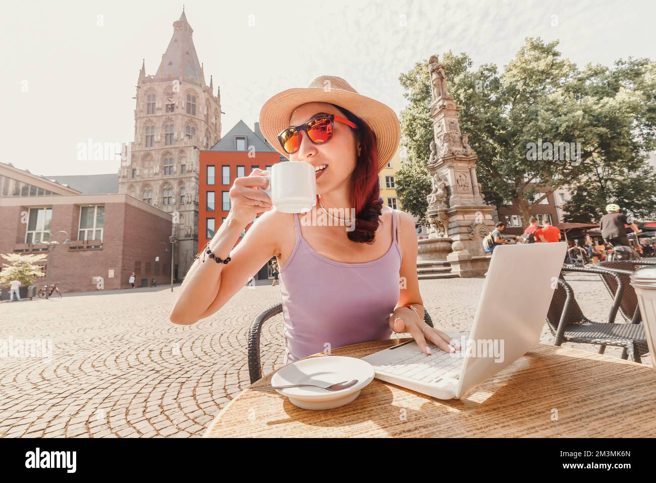 A girl drinks coffee in an old European city of Cologne and works or studies on a laptop. Remote employment and student life Stock Photo