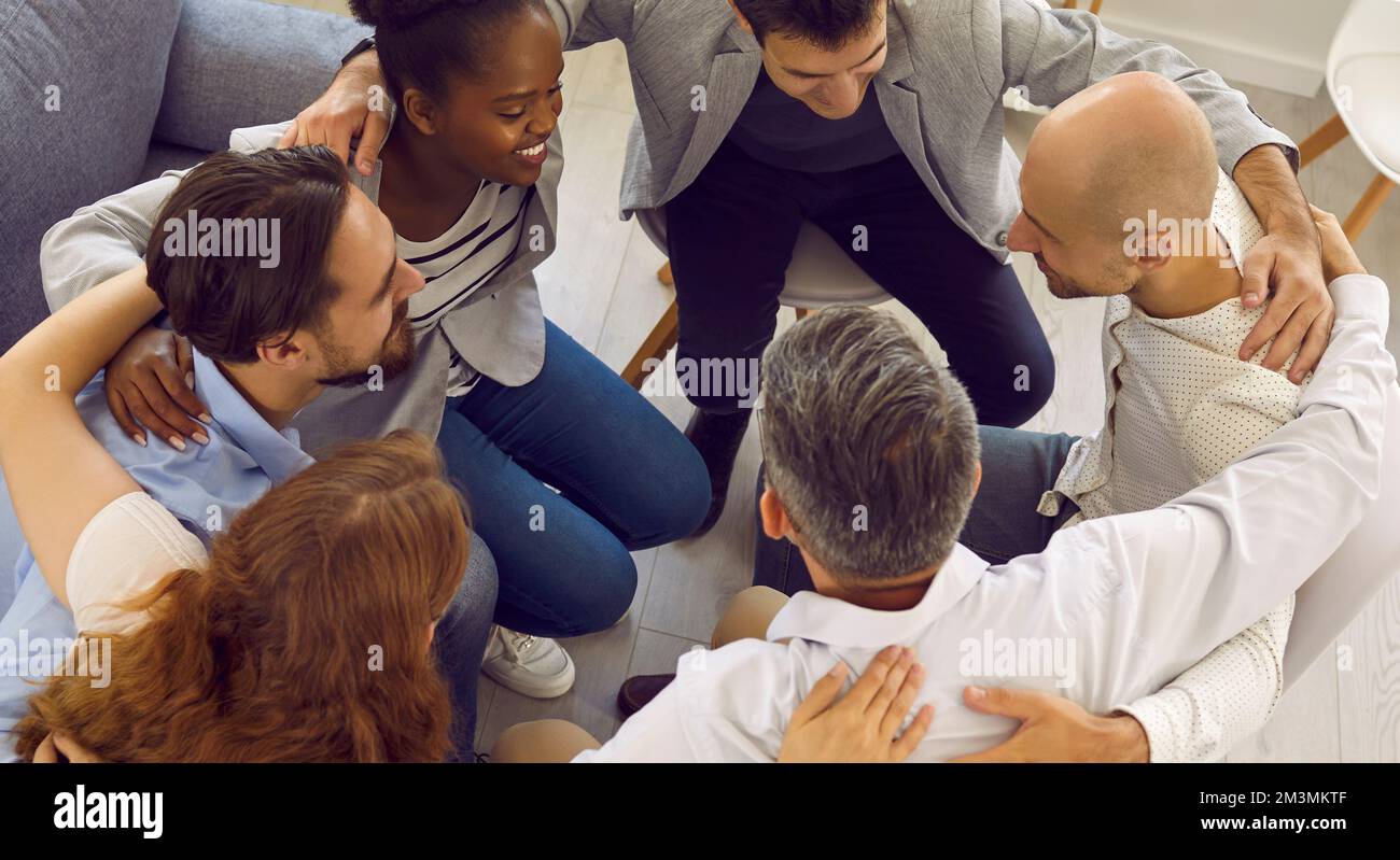 Multiracial people sit in circle hugging show unity at group psychological or counselling session. Stock Photo