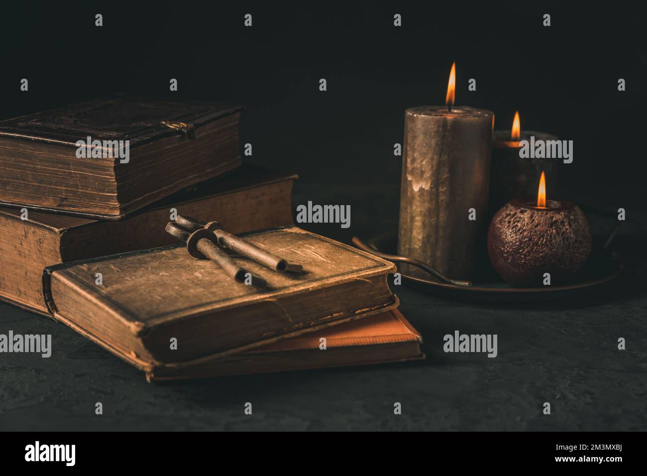 Pile of old antique books with candle and old rusty keys in vintage style on black background Stock Photo
