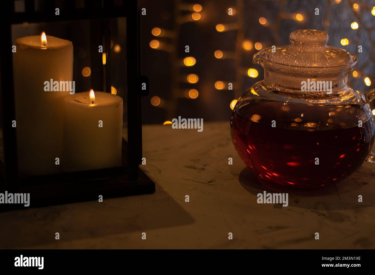 photo glass kettle with tea next to candles on a gray table Stock Photo