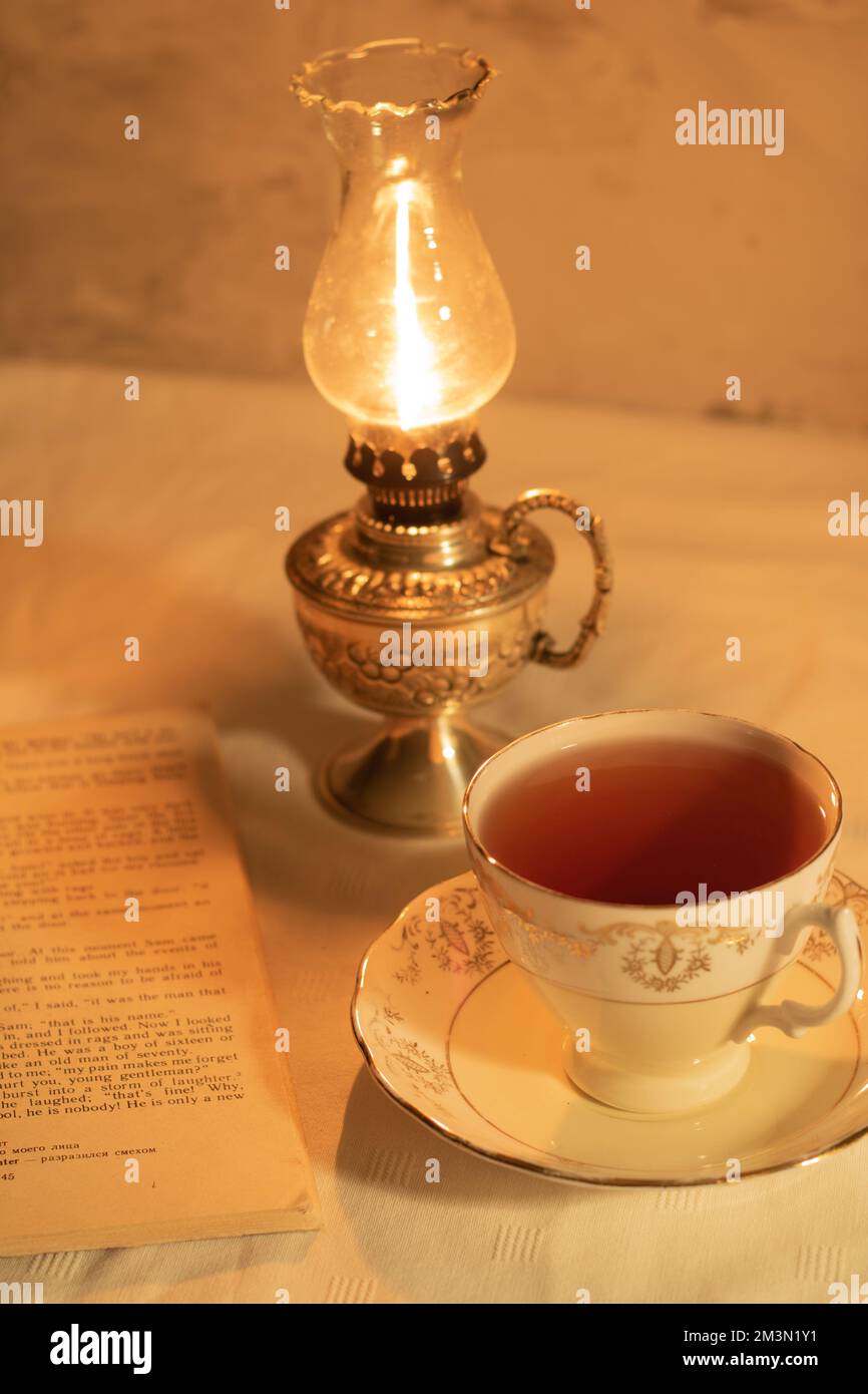 photo retro cup of tea with an old book next to a burning cerazine lamp Stock Photo