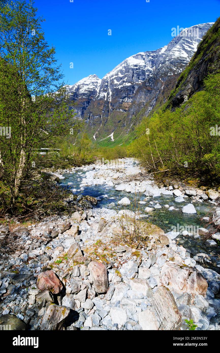 Clear water from glacial meltwater from the Kjenndalsbreen glacier passing snow capped mountains in the Lovatnet valley.. Olden, Norway Stock Photo