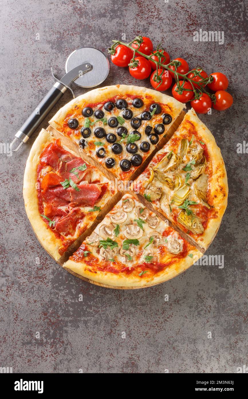 Pizza Four Seasons with Mozzarella cheese, ham, tomato sauce, mushroom, artichokes and olives closeup on the board on the table. Vertical top view fro Stock Photo