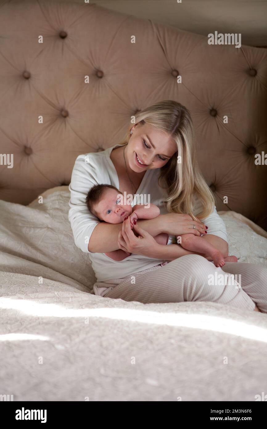 Mother sitting and holding sleeping newborn baby in arms at home in