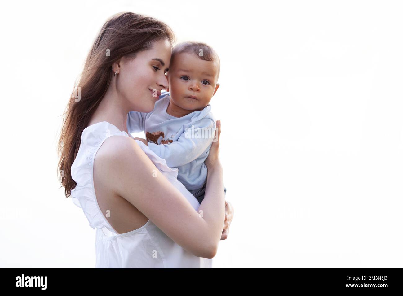 Mother hugs and holds child in her arms isolated on white background. Beautiful multiracial family Stock Photo