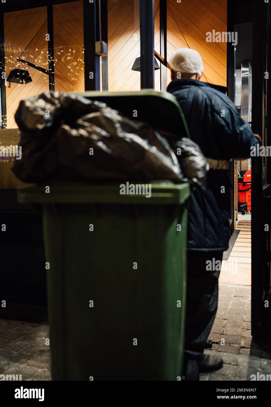 Man worker taking out a loaded green garbage bin waste trash and recycling from bar at christmas.  Stock Photo