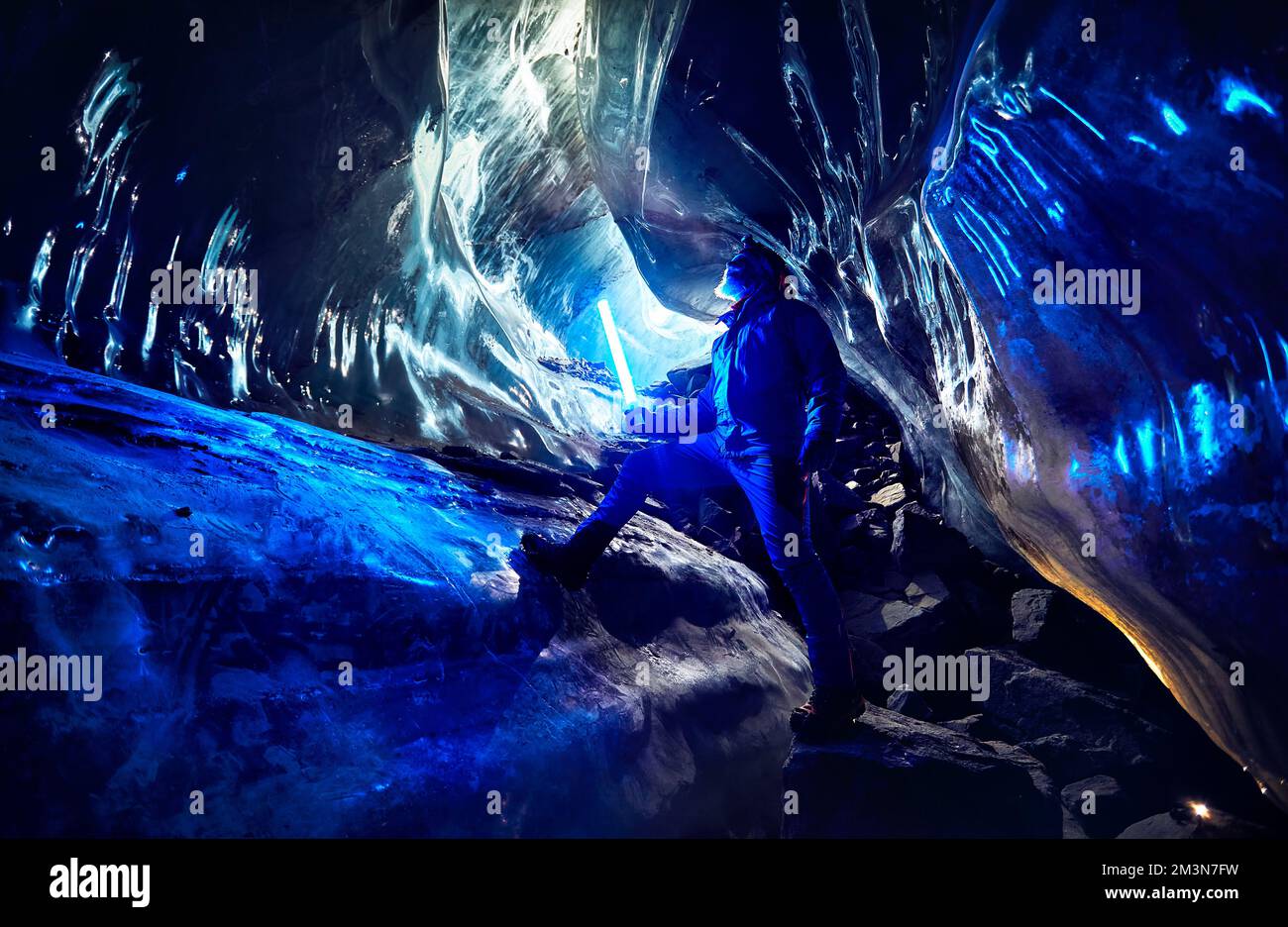 Tourist with grey beard with blue glowing led light is exploring an amazing glacial ice cave in the mountains of Kazakhstan Stock Photo