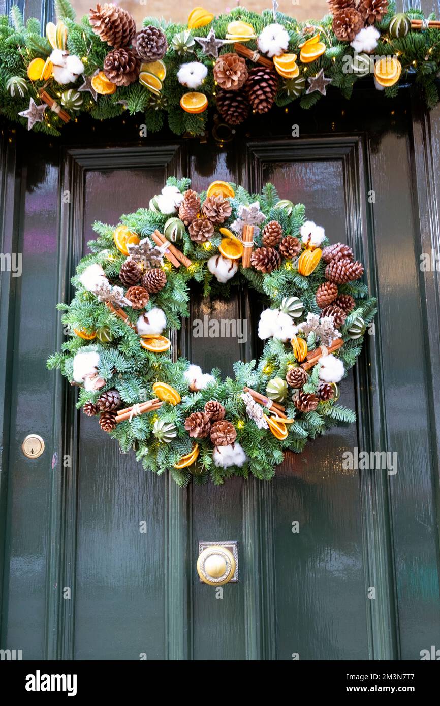 Christmas Xmas spruce wreath with pine cones cinnamon sticks and orange slices decorations hanging on green door London England UK KATHY DEWITT Stock Photo