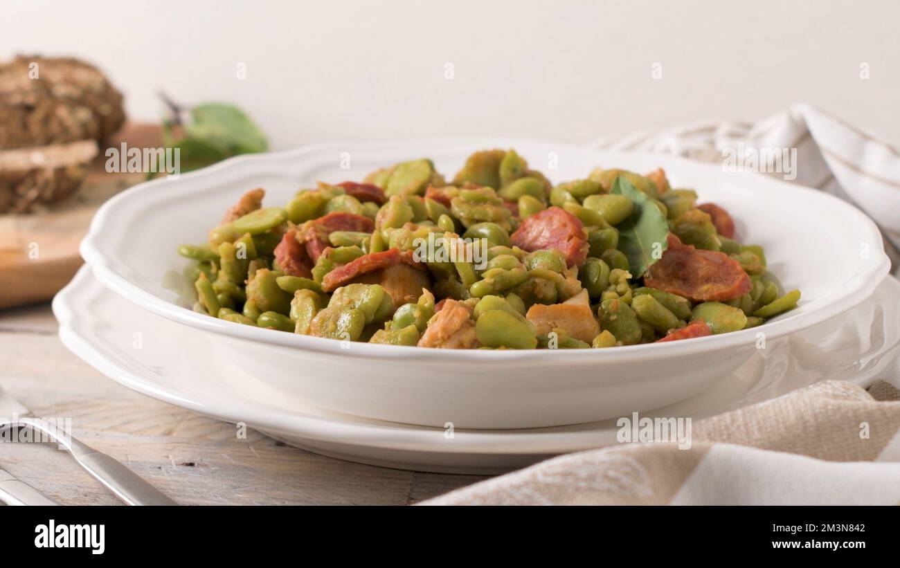 Boiled broad bean with chorizo and laurel leaves on a white ceramic